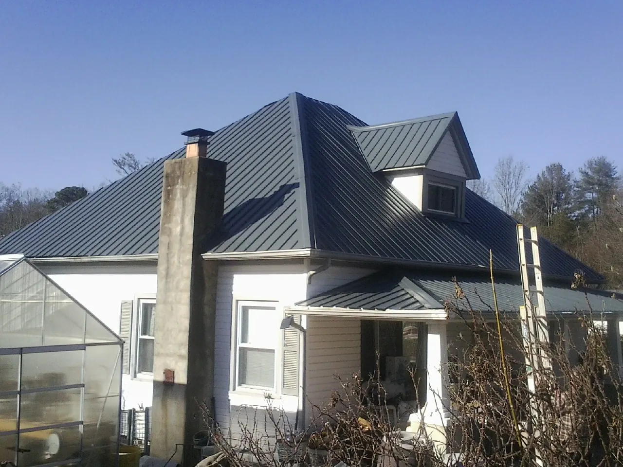 Dark blue standing seam metal roof on a white farmhouse with dormer — Slate & Tile Roof Repair by Roofing Brothers in Clatonia