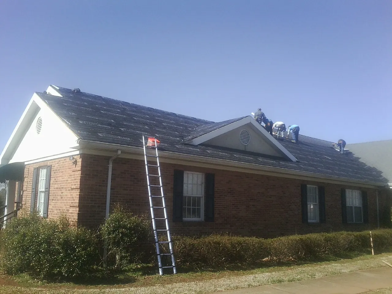 Crew tearing shingles off a brick ranch roof with a ladder set — Emergency Roof Repair work by our crew in Clatonia
