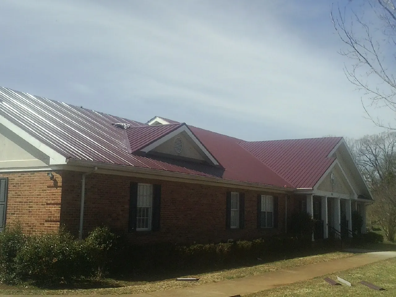 Red metal roof with gabled entries on a long brick building, from a Hail Damage Roof Repair job in Clatonia