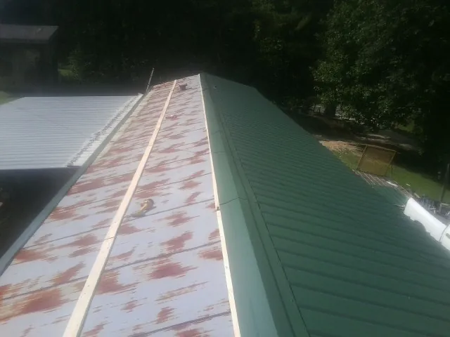 Old rusted panels beside newly installed green metal roofing — Wind Damage Roof Repair by Roofing Brothers in Clatonia