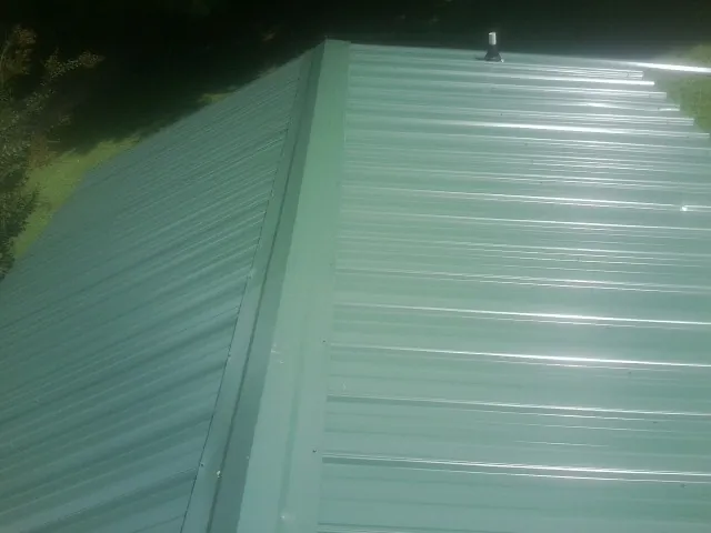New green metal panels meeting at the ridge of a roof — Flat Roof Repair work by our crew in Clatonia