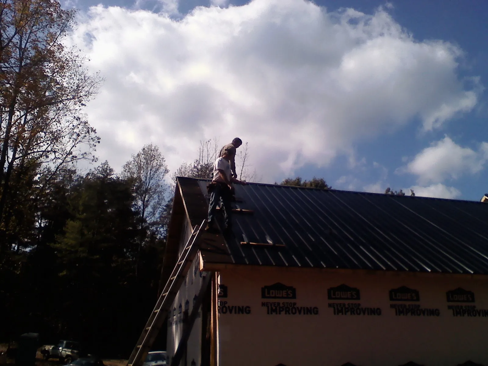 Roofer fastening dark metal panels high against a cloudy sky, from a Roof Inspection job in Clatonia