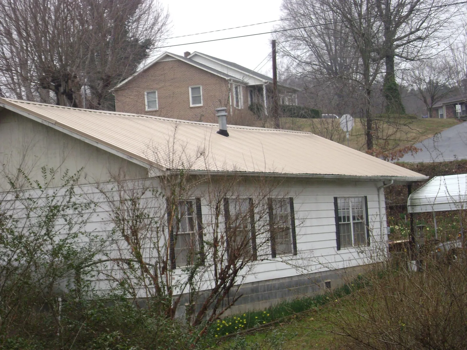 Tan metal roof on a white sided house set into a hillside — Commercial Roofing by Roofing Brothers in Clatonia