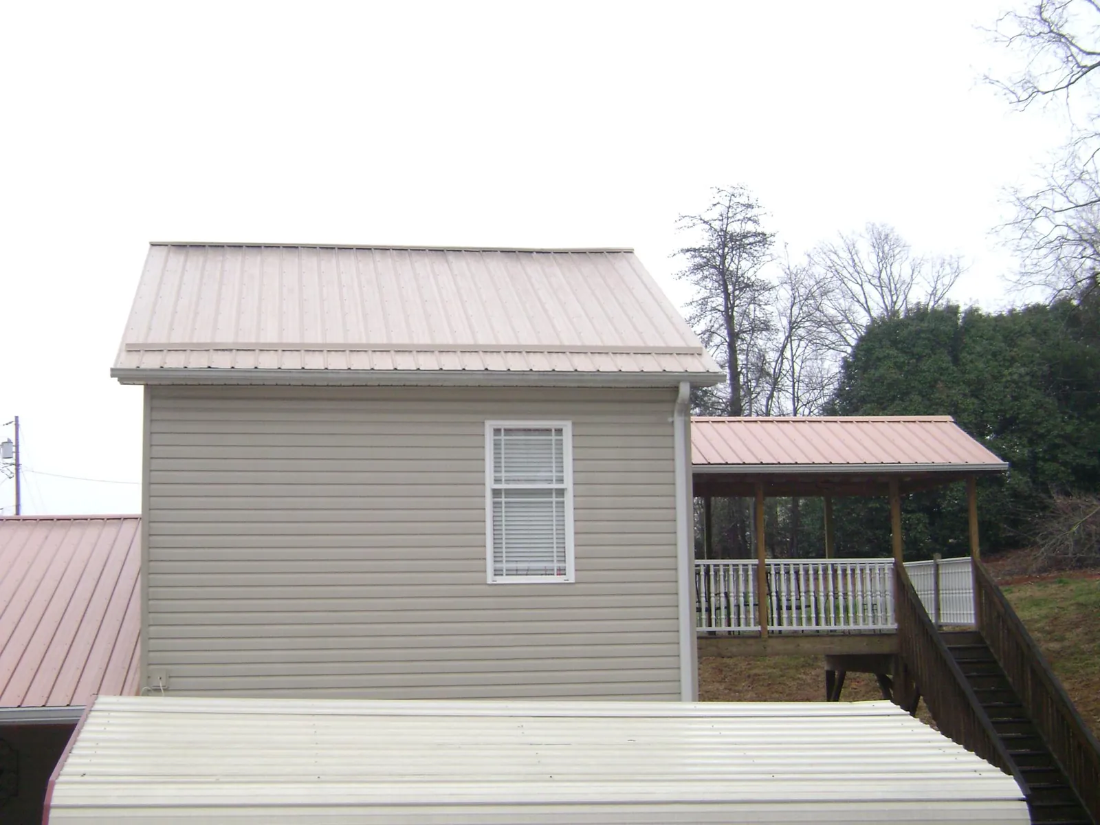 Tan metal roofs on a two story addition and attached porch, from a Roof Replacement job in Clatonia